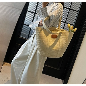Detail of beige woven straw tote bag with brown leather patch and large capacity