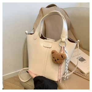 Detalle de bolso tipo cubo crema con colgante de oso y adorno de cuerda trenzada