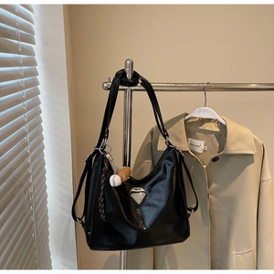 Detail of black leather tote bag featuring triangular metal plaque and baseball charm