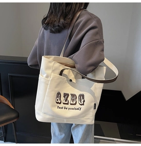 Dettaglio della borsa tote in tela con stampa QZBG e manici marroni portati a spalla