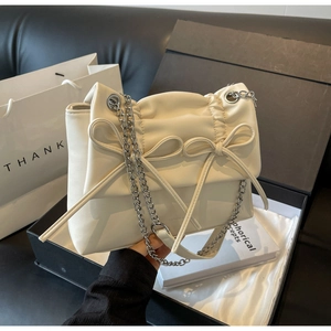 Detail of a creamy beige crossbody bag with pleated bow decor and silver chain strap