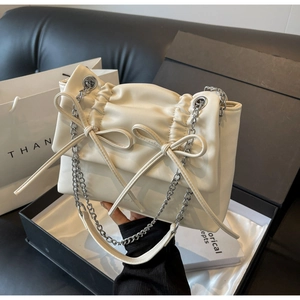 Detail of cream pleated crossbody bag with dual bow accents and silver chain strap