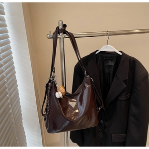 Detail of dark brown glossy leather tote bag with silver triangle logo and baseball charm