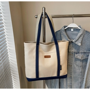 Canvas tote bag with blue trim and leather logo hanging against a natural lifestyle background