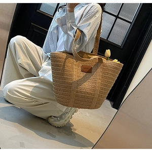 Detailed close-up of woven tote bag featuring a brown leather patch and natural khaki texture