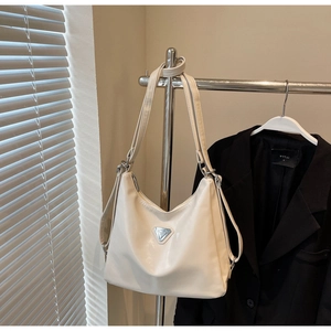 Detail of cream shoulder bag with metallic triangular logo and adjustable strap