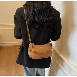 Detail view of brown leather half-moon crossbody bag with gold chain on back of model