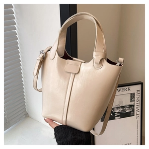 Detalle del bolso de cubo en cuero beige con asa gruesa y forro de color rojo oscuro