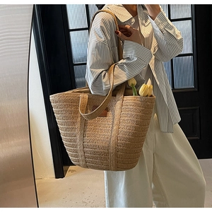 Detail of a large straw tote bag with natural woven texture and leather logo patch