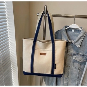 Detail of canvas tote bag showing reinforced blue handles and front pocket with leather logo