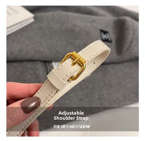 Macro shot of adjustable cream leather shoulder strap with gold metal buckle and stitching