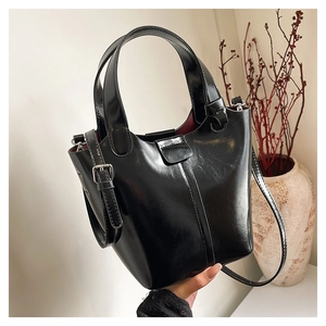 Detalle de bolso tipo cubo negro brillante con forro rojo oscuro y hebillas de plata