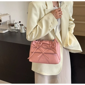 Pink crossbody bag with 3D bows and silver chain strap shown on a cream blazer outfit