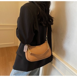 Close-up of brown textured croissant bag featuring gold chain strap and leather tag