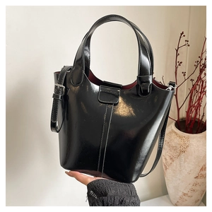 Detalle del bolso de cubo negro brillante con asa ancha y forro interior rojo