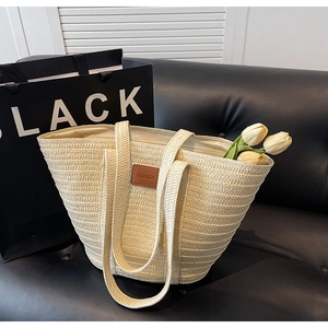 Detail of cream straw tote bag with brown leather label and shoulder straps