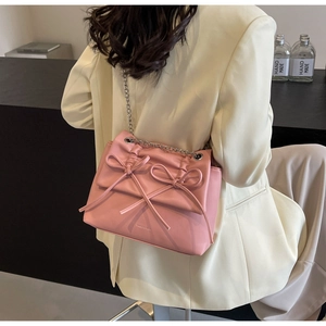 Close-up of pink bow shoulder bag with silver chain strap worn by a model