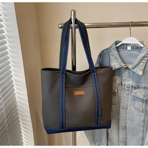 Detail of grey and navy canvas tote bag featuring leather logo and contrast stitching