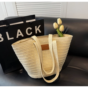 Detail of hand-woven straw tote with leather patch and tulips on a black sofa