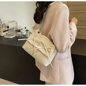 Chic beige bow-knot crossbody bag with silver chain strap shown in a modern cafe setting