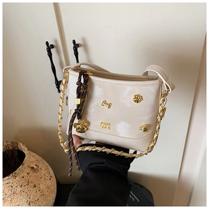Detail of cream glossy leather tote featuring golden dog-themed charms and metal hardware