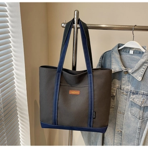 Detail shot of grey canvas tote bag with navy blue straps and branded leather patch