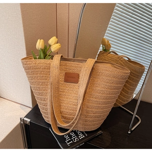Detail of handwoven straw tote bag with brown leather patch and slim shoulder straps