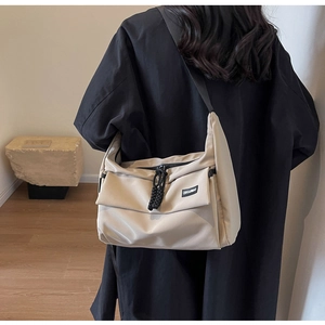 Detail van beige nylon schoudertas met zwarte rits en verstelbare riem op een model