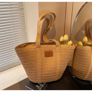 Detail of hand-woven straw tote bag with brown leather patch and wide woven handles
