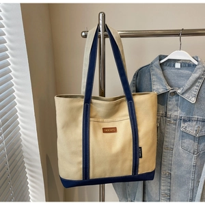 Detail of canvas tote bag showing navy blue strap contrast and brand leather label