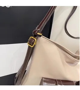 Détail de la boucle en métal doré et de la bandoulière en cuir marron sur le sac crème