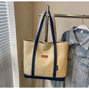 Close-up of contrast canvas tote bag with leather logo patch and metal handle detail