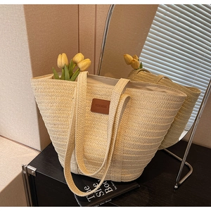 Detailed close-up of woven straw texture and brown leather patch on beige tote bag