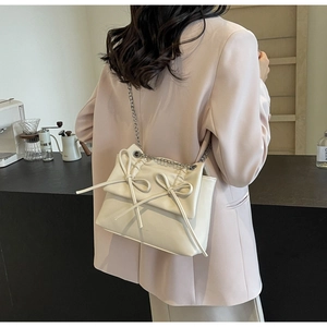 Side view of a beige crossbody bag with bow accents and silver chain strap