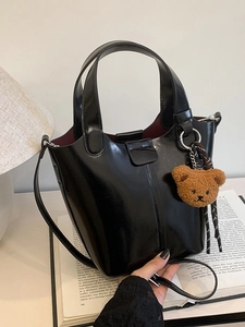 Bolso tipo cubo negro brillante con colgante de oso, asas y correa de hombro ajustable