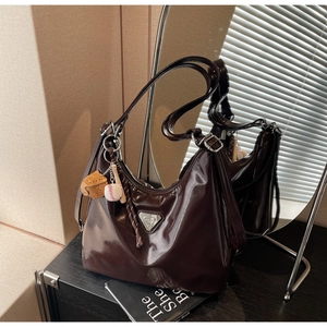 Close-up of glossy brown tote bag with metal triangle logo and baseball charm detail
