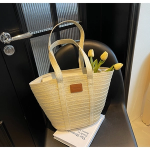 Close-up of straw woven tote bag with leather logo tag and yellow tulips on a chair