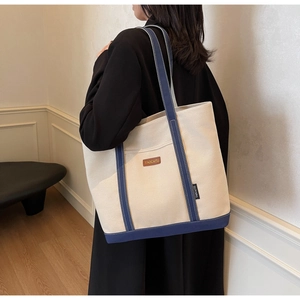 Detail view of cream canvas tote bag with navy blue straps shown on model in a cozy room