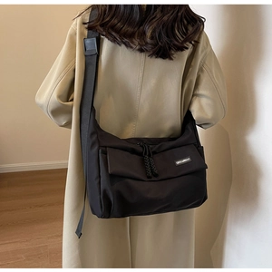 Detail van zwarte nylon schoudertas met verstelbare riem en wit merklogo-label