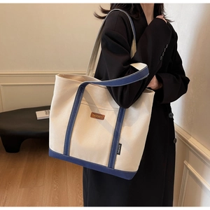 Detail of canvas tote bag with deep blue straps and logo patch worn by model