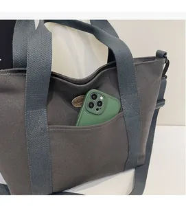 Detail shot of a dark grey canvas tote bag front pocket holding a green smartphone
