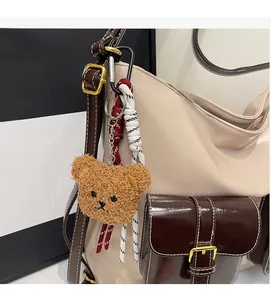 Détail d'un porte-clés ours en peluche marron avec cordes sur un sac à bandoulière