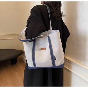 Close-up of large canvas tote bag showing side leather tag and grey-blue color design