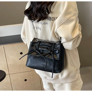 Detail of black crossbody bag featuring bow accents and silver chain strap on model