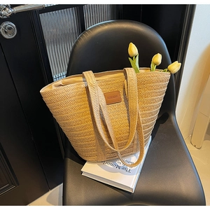 Close-up of straw tote bag with leather logo tag placed on a chair with tulips