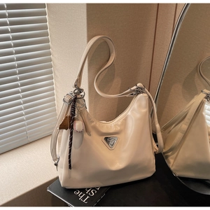 Detail of a beige glossy hobo bag with silver logo and sporty keychain on a window sill