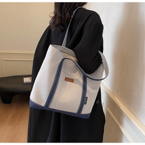 Close-up of large canvas tote bag with navy blue trim and leather logo patch