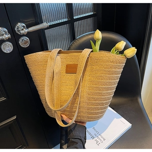 Detail of a woven straw tote bag with a leather logo plate on a dark textured surface