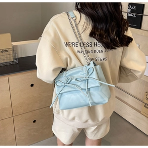 Detail of light blue crossbody bag featuring decorative bows and silver chain strap