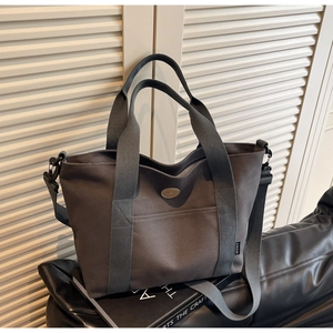 Close-up of grey canvas tote bag with adjustable shoulder strap on a black leather cushion